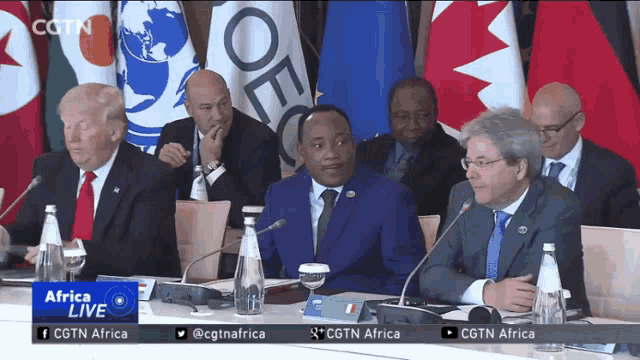 a group of men are sitting at a table with microphones and flags behind them and the words africa live on the bottom