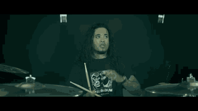 a man with long hair is holding a pair of drum sticks