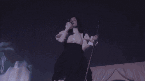 a woman singing into a microphone with her hands up