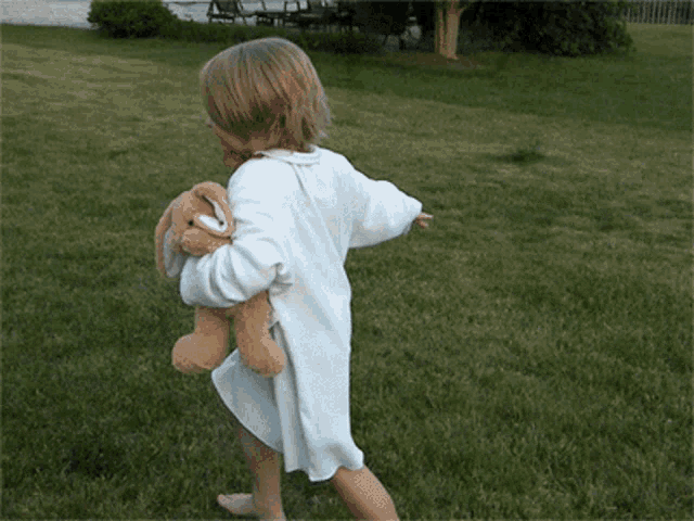 a little girl in a white dress is holding a stuffed bunny rabbit