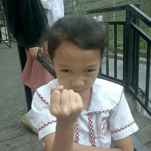 a little girl in a school uniform is sitting on a bench making a funny face .