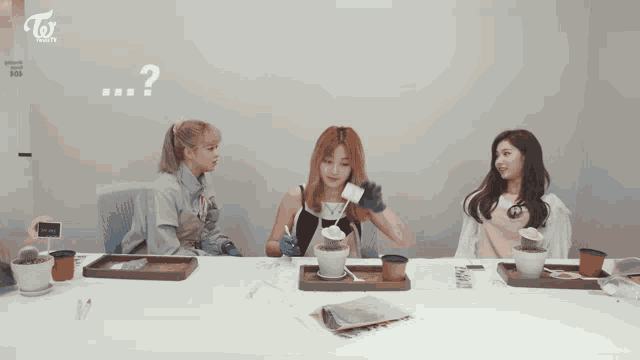 three women are sitting at a table with a question mark on the wall above them