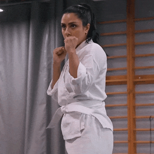 a woman in a white karate uniform is standing in front of a curtain