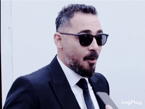 a man with a beard wearing sunglasses and a suit has the word imgplay on the bottom