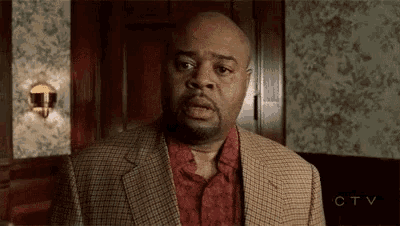 a man in a suit and red shirt is making a surprised face .