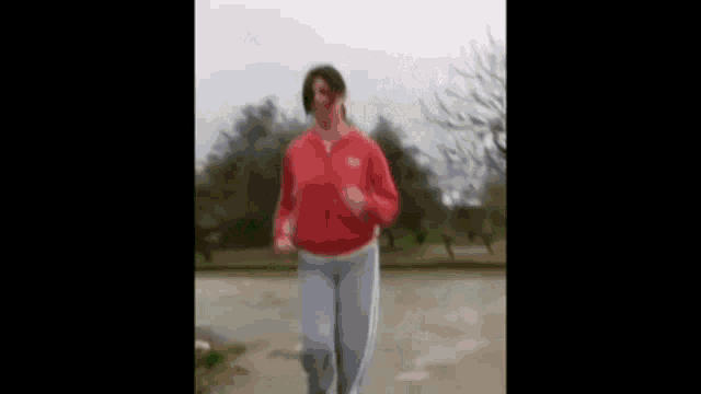 a woman in a red jacket and grey pants is jogging