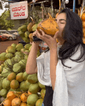 a woman drinking from a coconut in front of a sign that says ' aaradh ' on it