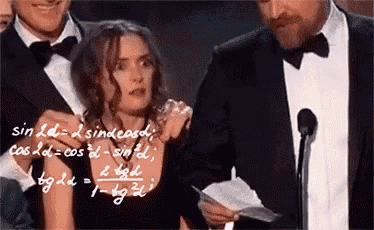 a man in a tuxedo is holding a piece of paper in front of a woman in a dress .
