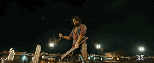 a man with a beard is holding a bat in a dark room with xhk written on the bottom right corner
