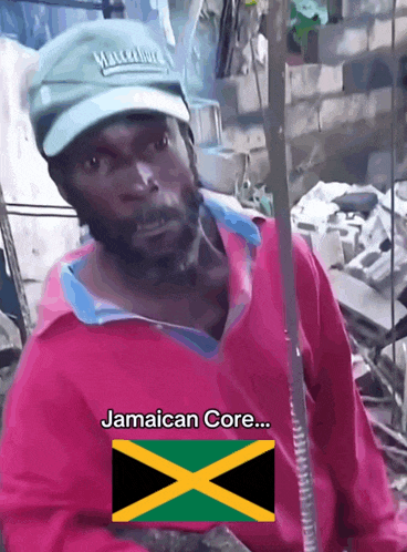 a man wearing a green hat and a pink shirt has the jamaican core written on his chest