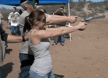a woman in a tank top is holding a large gun