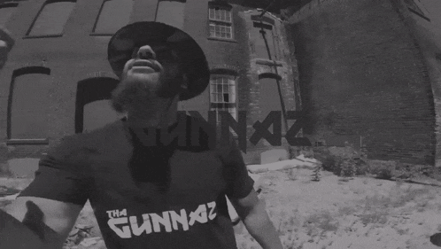 a man wearing a gunnaz shirt stands in front of a building