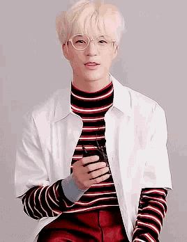 a young man wearing glasses and a striped turtleneck is holding a cell phone .