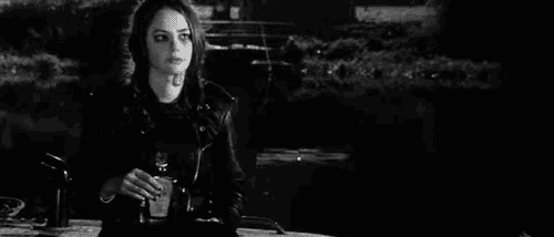 a woman in a leather jacket is sitting on a bench drinking from a bottle .