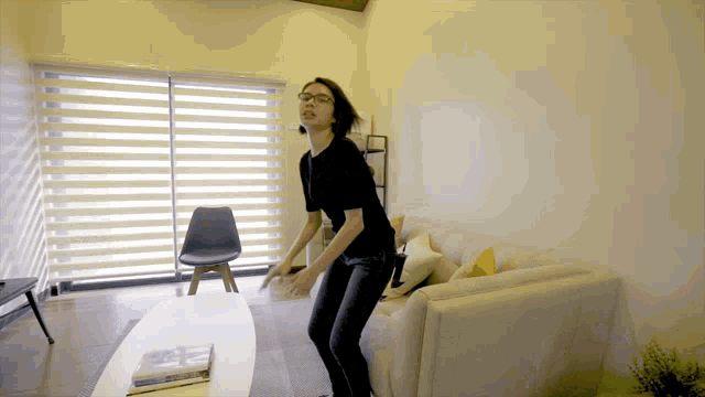 a woman wearing glasses is dancing in a living room with a white couch