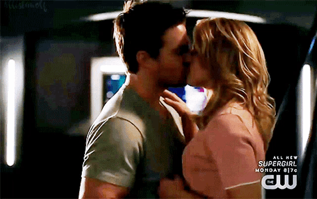 a man and a woman are kissing in front of a sign that says supergirl on it