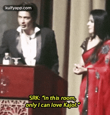 a man in a tuxedo stands next to a woman in a red dress and says srk : in this room