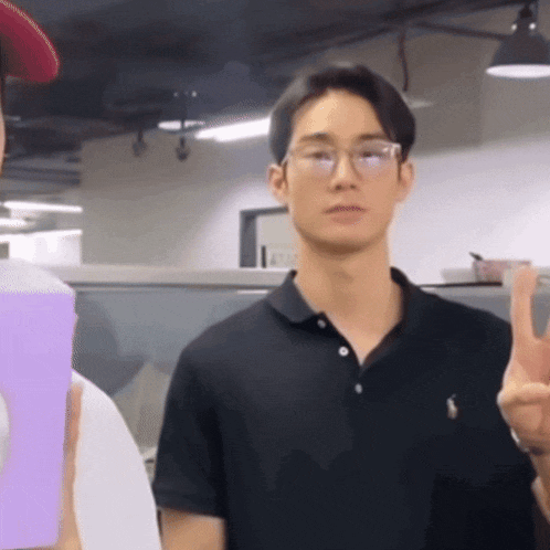 a man wearing glasses and a black polo shirt giving the peace sign