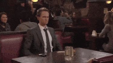 a man in a suit and tie is sitting at a table in a bar .