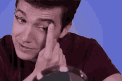 a man is touching his eye with his finger while looking at something .