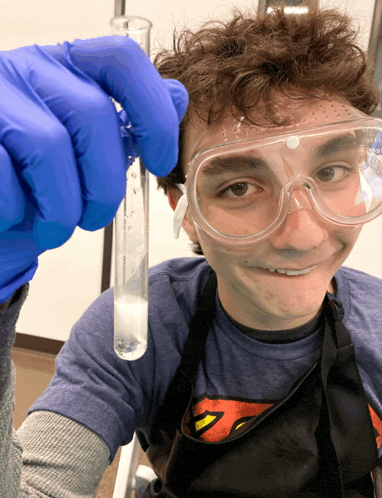 a young man wearing a superman apron and goggles holds a test tube