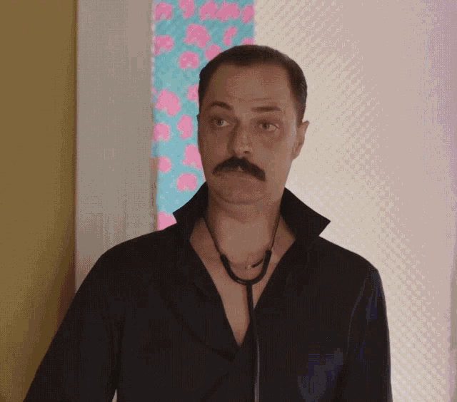 a man with a mustache wearing a black shirt and a stethoscope around his neck