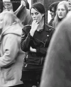 a black and white photo of a woman wearing a leather jacket standing in a crowd of people .