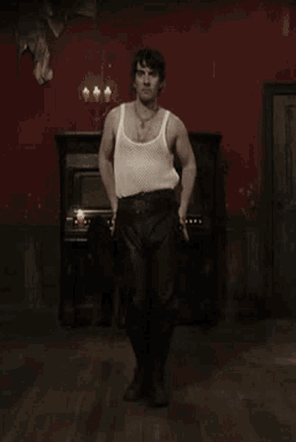a man in a white tank top is standing in a room