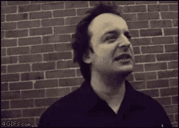 a man in a black shirt is standing in front of a brick wall and making a funny face .