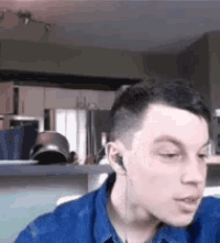 a man wearing a blue shirt and ear buds is sitting in a kitchen .