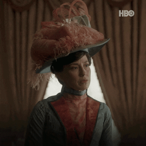 a woman wearing a feathered hat says " what can i do " in white letters