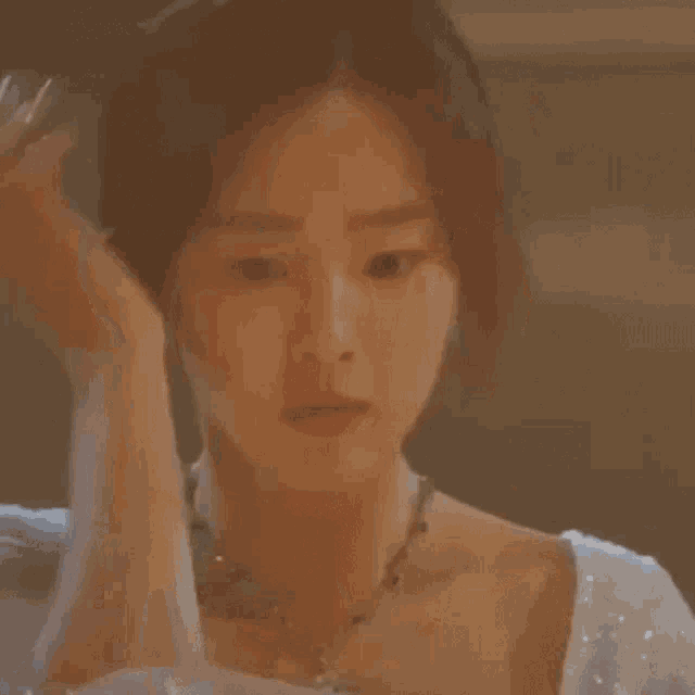 a woman in a white dress and necklace is adjusting her hair .
