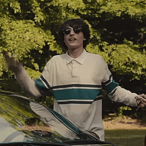 a man wearing sunglasses and a striped shirt stands in front of a car