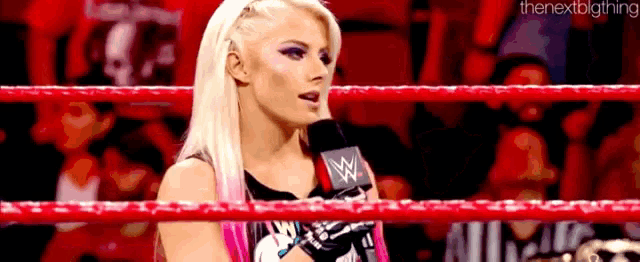 a woman is standing in a wrestling ring with a microphone .