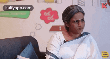 a woman in a white saree is sitting on a couch and making a face .