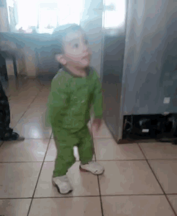 a little boy in a green outfit is dancing on a tiled floor