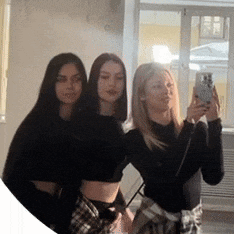 three women are standing next to each other in front of a mirror taking a selfie .
