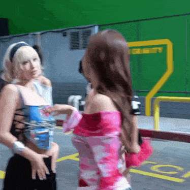 two women are standing next to each other in a parking lot with a green screen in the background .