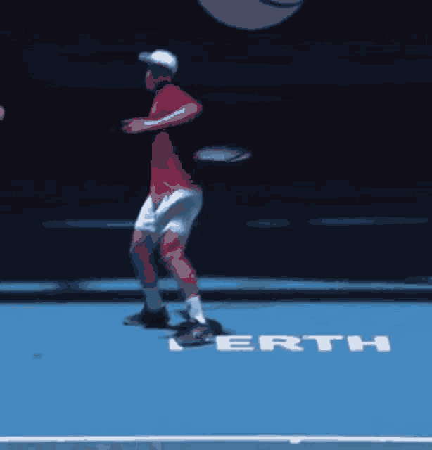 a man in a red shirt is playing tennis on a blue court with the word perth written on it