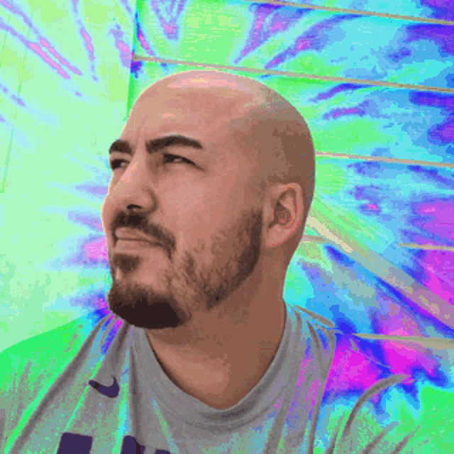 a bald man with a beard is wearing a grey shirt with the letter l on it
