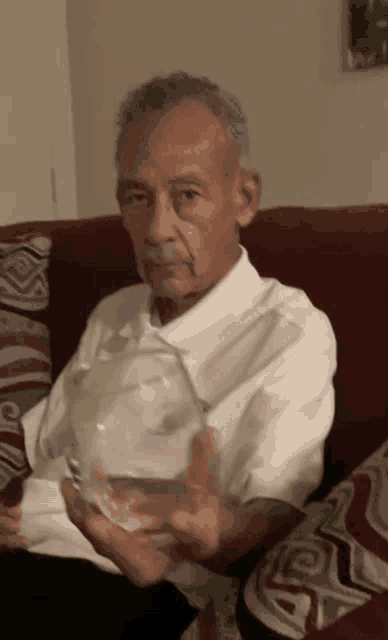 an elderly man sitting on a couch holding a glass
