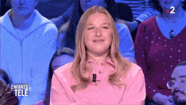 a woman in a pink shirt is smiling in front of a children 's tele audience