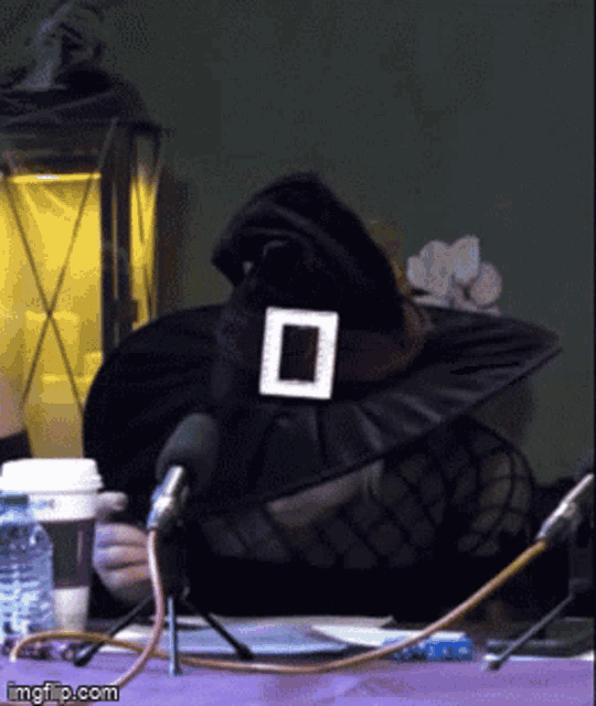 a woman wearing a witch hat is sitting at a table with microphones and a cup of coffee