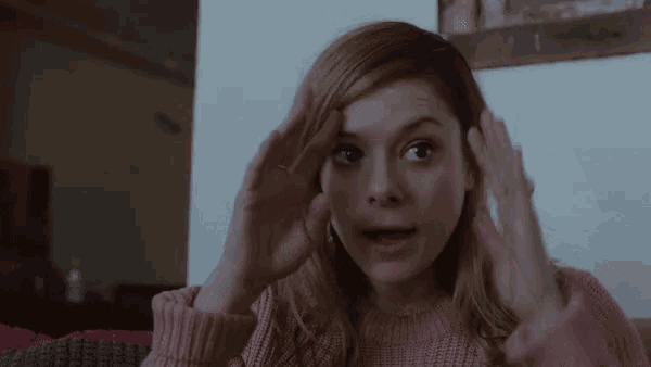 a woman wearing a pink sweater is covering her ears with her hands
