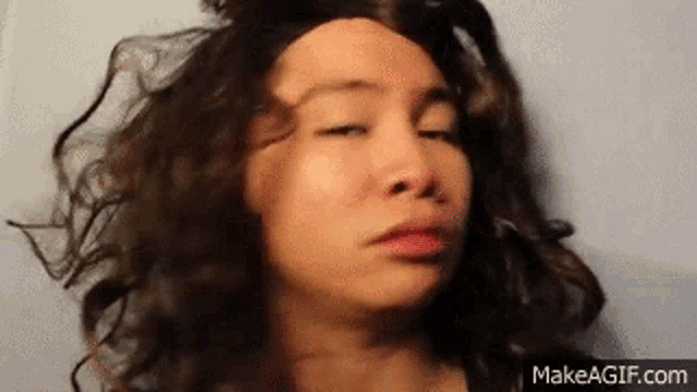 a woman with curly hair is making a funny face with her eyes closed .