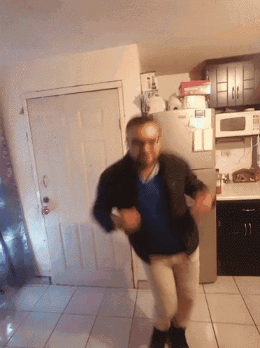 a man is dancing in a kitchen in front of a refrigerator that has a note on it