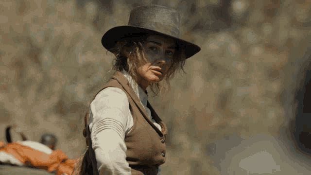 a woman wearing a hat and vest is sitting on a horse