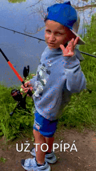 a young boy is holding a fishing rod and giving a peace sign in front of a lake