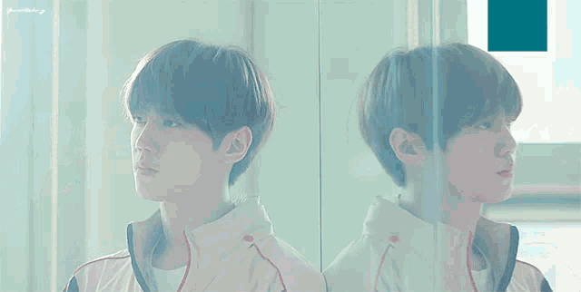 a boy drinking water from a bottle with a reflection of him in the mirror