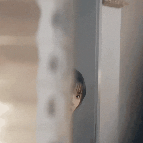 a woman is peeking out from behind a door and looking at the camera .